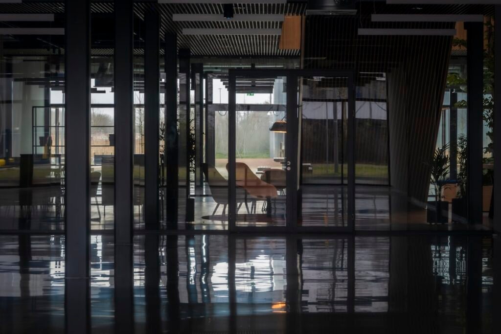 Dimly lit modern office interior with glass partition walls, chairs and reflections on a polished dark floor