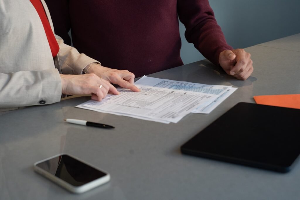 Two people at a grey meeting table, one pointing at a printed financial statement between them