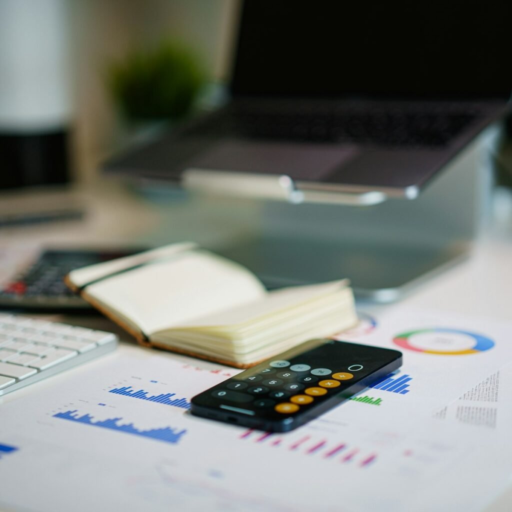 Printed bar and donut charts spread across a desk beside an open notebook, a calculator and a laptop