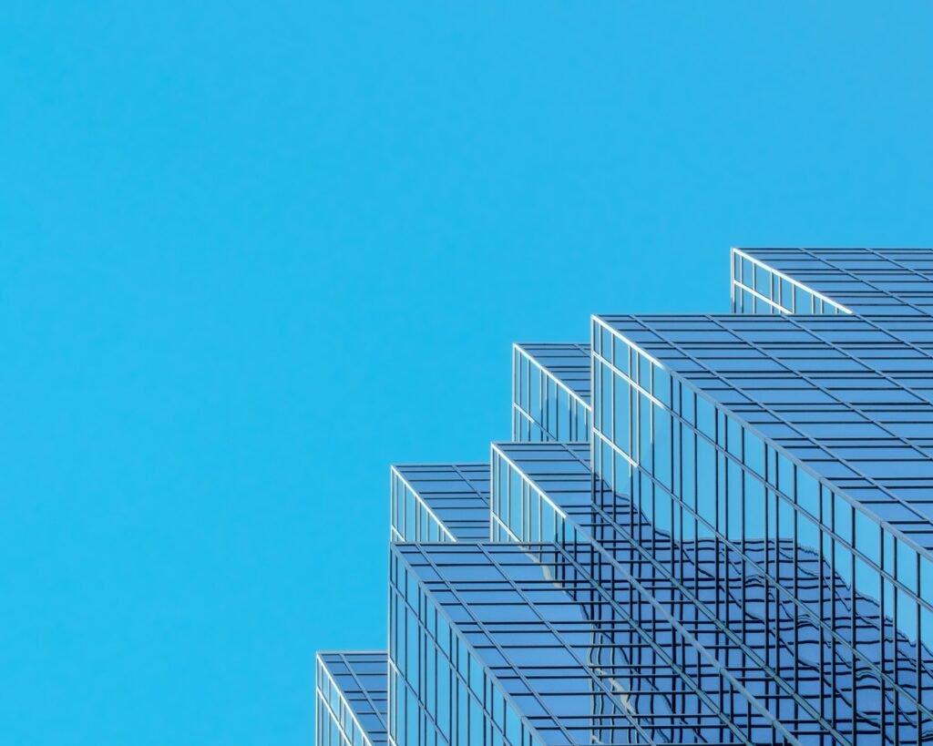 Upper corner of a stepped blue-glass office tower against a clear sky, its facade rising to the right